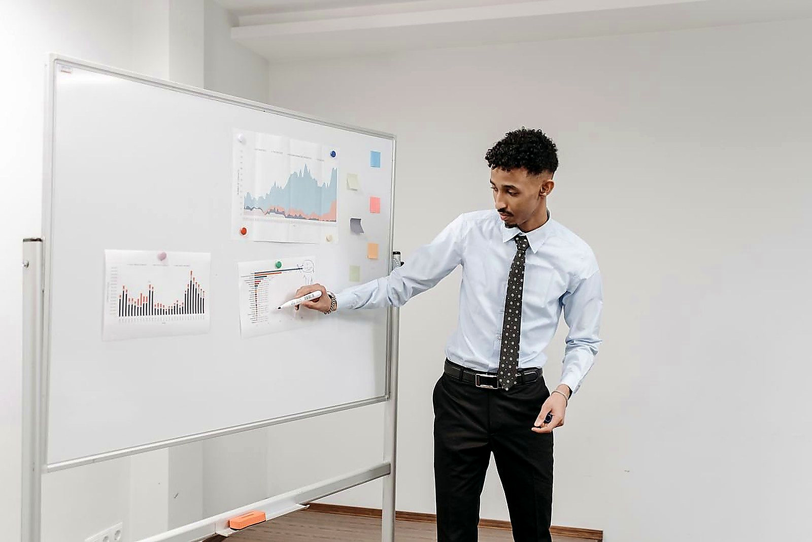 Free Man presenting charts on a whiteboard during a business meeting in a contemporary office. Stock Photo