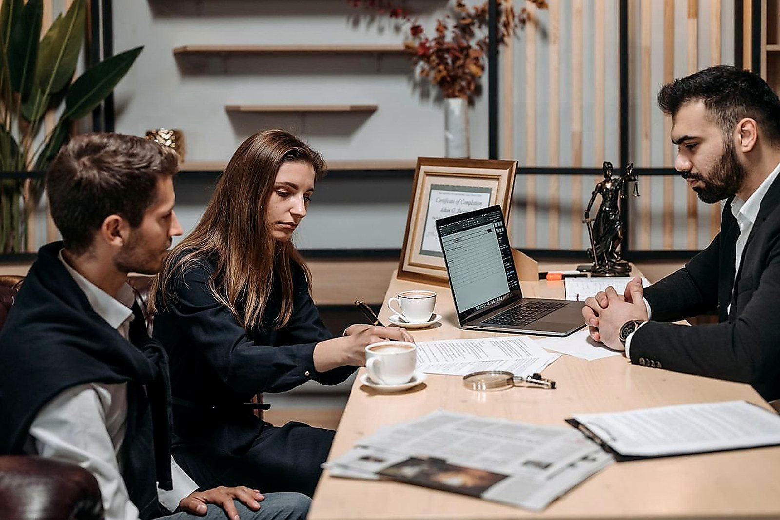 Free Three professionals discussing documents over coffee in a modern office setting. Stock Photo