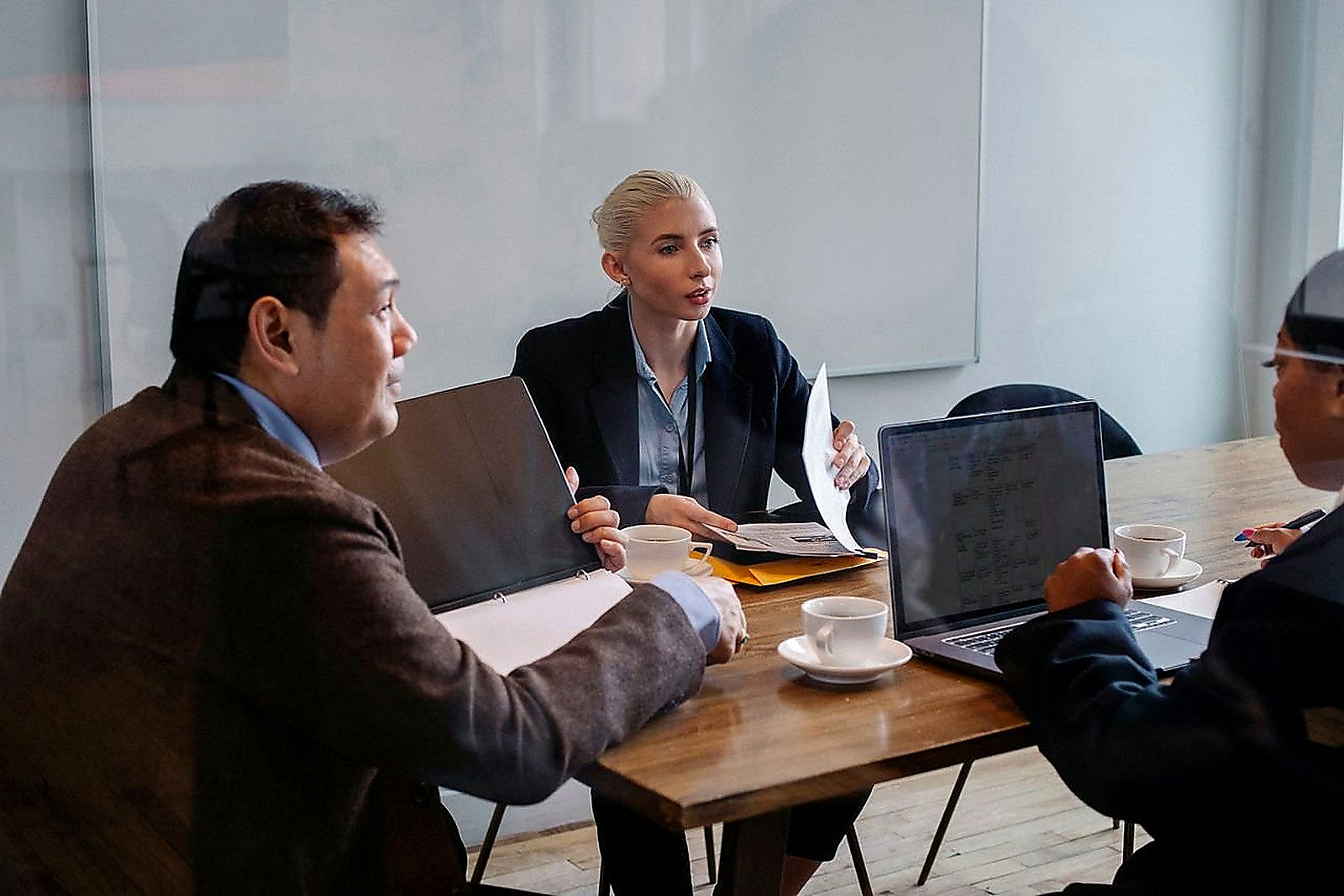 Free Multiracial colleagues in formal clothes sitting at table with laptop and documents while discussing details of business plan Stock Photo