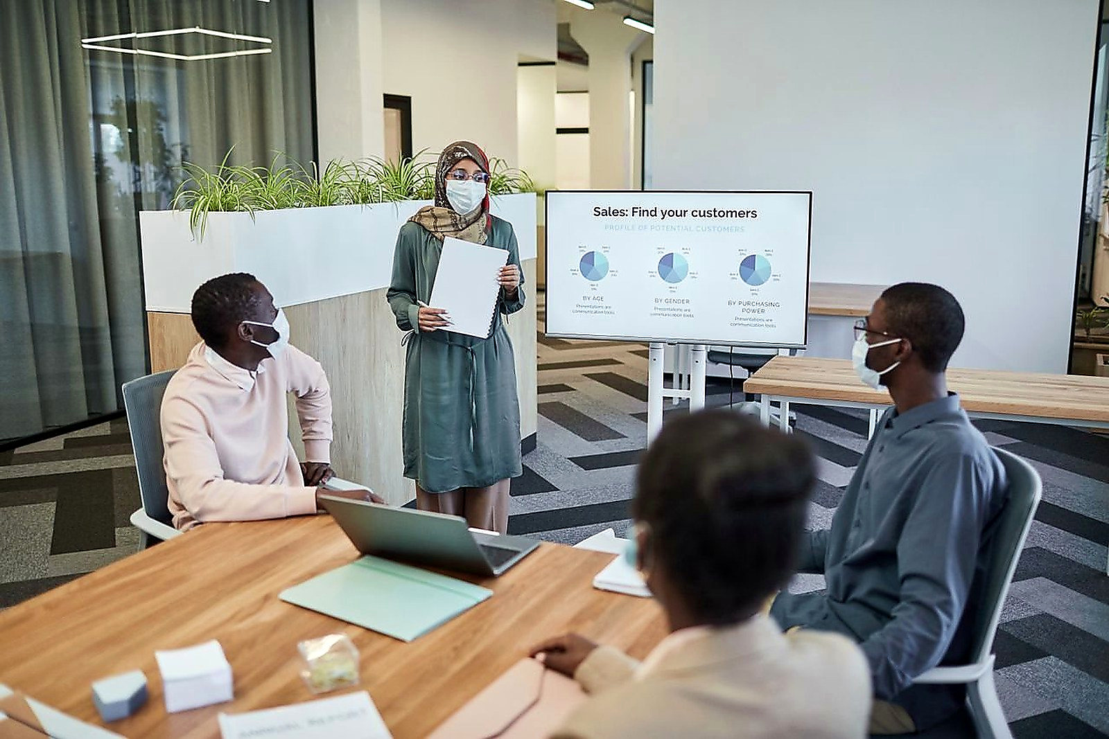 Free Colleagues wearing masks in a modern office discussing sales strategies. Stock Photo